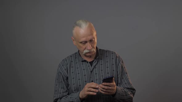 Senior Man with Grey Ponytail Holds Smartphone and Shocks