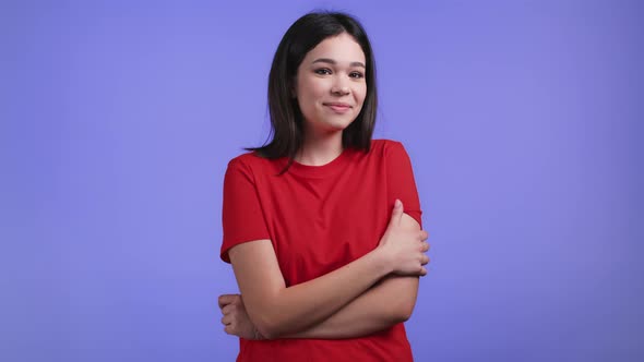 Young Modest and Shy Woman in Orange Tshirt Looking to Camera on Violet Studio Background