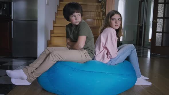 Wide Shot Argued Brother and Sister Sitting Back to Back on Bag Chair Indoors