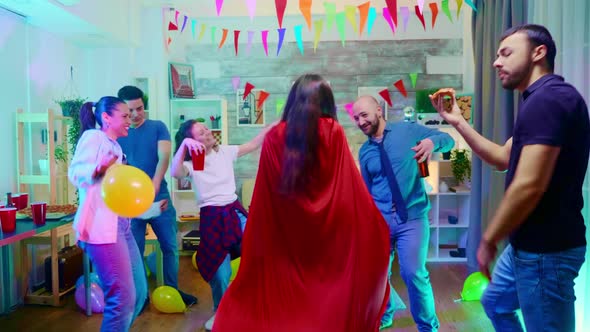 Zoom in Shot of Girl Dressed Up Like a Superhero with Red Cape at Her Friends Party.