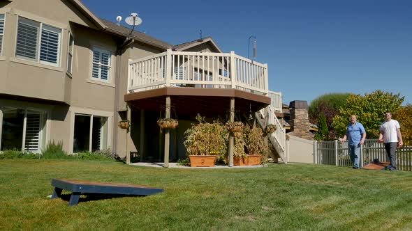 Father and son playing cornhole in the back yard; static, wide angle view of the game in progress