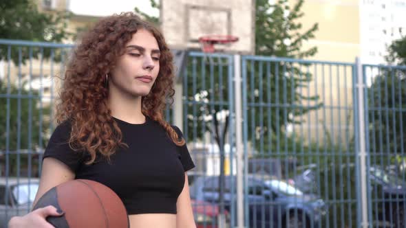 Portrait of a Young Beautiful Active Woman with a Ball on a Street Basketball Court