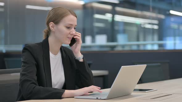 Businesswoman Talking on Smartphone While Using Laptop