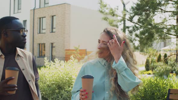 Multiethnic Man and Woman Walking with Coffee in Park and Talking