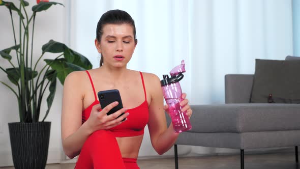 Sportive Woman Drink Water After Active Workout Exercise Uses Smartphone at Home