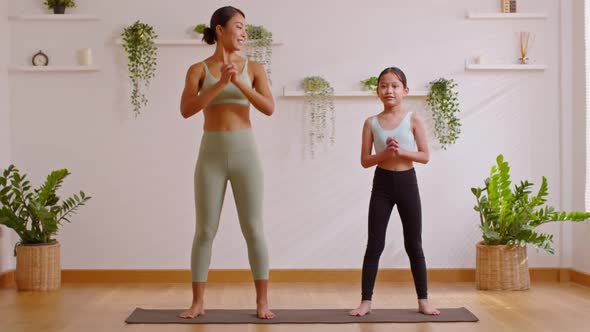 Healthy couple mom and little girl doing yoga squat up and down on mat at home.Mother and female dau