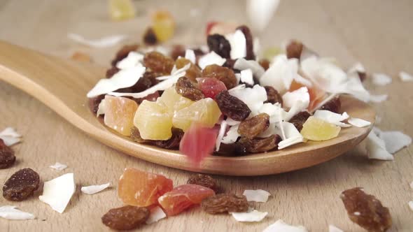 Dried pieces of tropical fruit mix fill a wooden spoon on a board