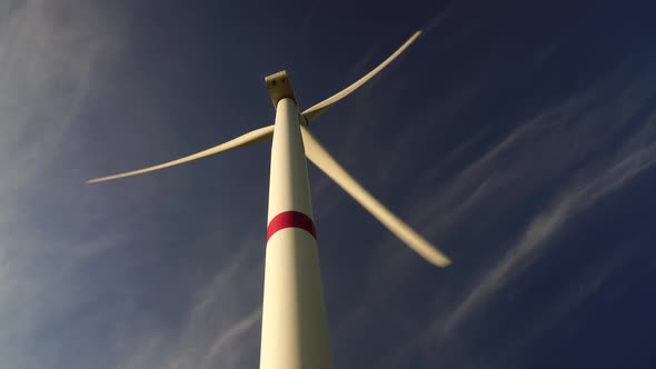 Blades of a Large Wind Turbine in a Field Against a Background of Cloudy Blue Sky on the Horizon