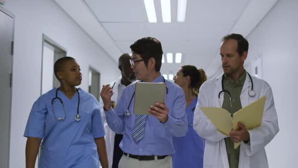 Diverse group of male and female doctors talking in hospital corridor, walking with tablet and file