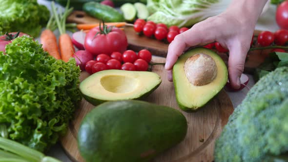 Hand Putting Cut Avocado On Table With Fresh Vegetables