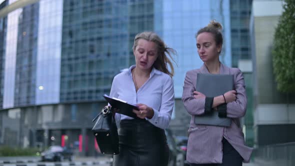 Two young business women communicate while walking on the street