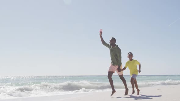 Smiling african american father with son flying kite on sunny beach