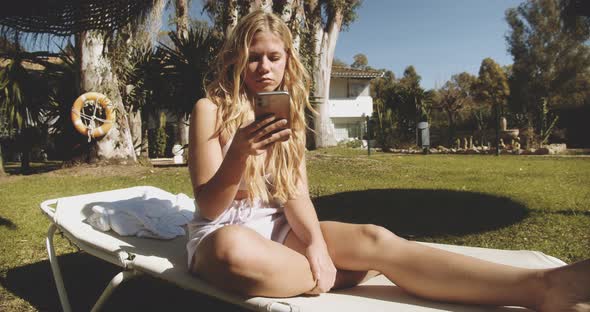 Woman Sitting On Sun Lounger And Texting On Smartphone