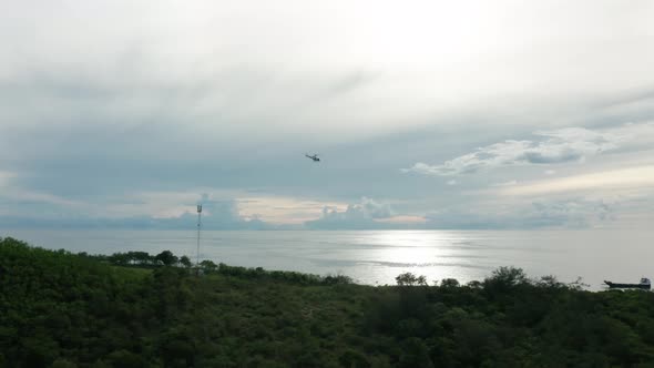 Helicopter flying away from tropical island towards barge for next supply run