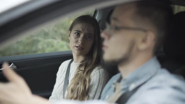 Portrait of Unhappy Young Caucasian Woman Sitting on Passenger Seat Talking To Man Driving