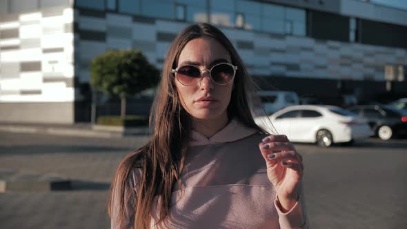 Portrait of Beautiful Young Woman with Glasses Looking Into Camera in Slow Motion As Wind Blows Her