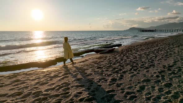 A girl in a yellow coat walks on the beach 4 K Aerial View