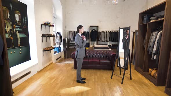Young man checking himself in boutique mirror while trying on suit.
