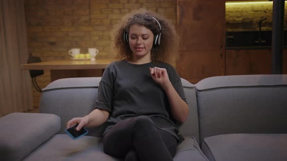 Young Millennial Female Adult Switches on Music on Mobile Phone and Enjoys in Headphones