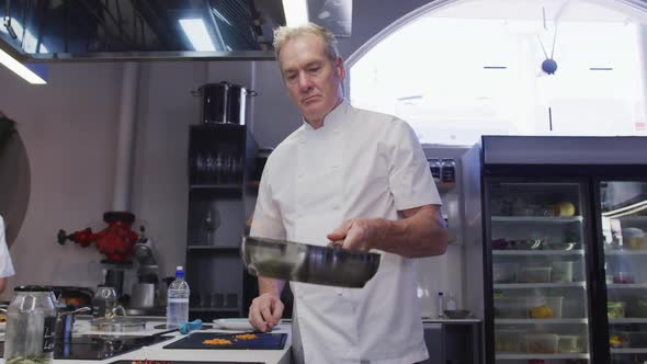 Professional Caucasian male chef in a restaurant kitchen preparing food using a frying pan