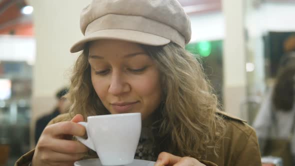 Portrait of a Beautiful Girl Drinking a Cup of Coffee on the Veranda in a Summer Cafe in a Newsboy