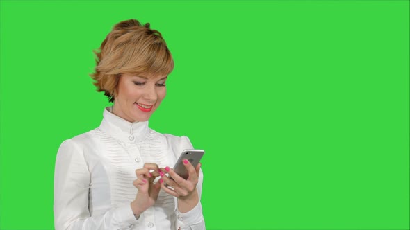 Young Attractive Woman Works on Smartphone and Smiles on a Green Screen, Chroma Key
