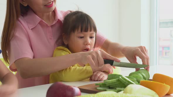 Enjoy Asian mom teaching a little daughter holding knife cut fresh vegetables, Happy family mother a