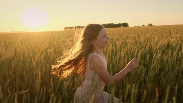 Little Girl with Long Hair Runs Across the Field at Sunset