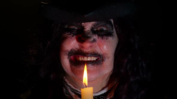 Sinister Woman with Scary Halloween Witch Makeup in Costume Making Voodoo Magic Rituals with Candle