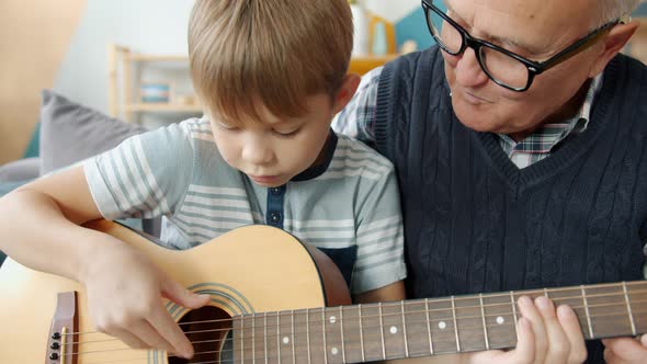 Caring Grandfather Helping Cute Kid Teaching Guitar Playing at Home Together
