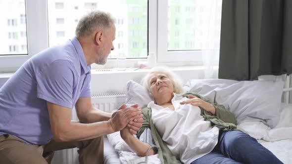 Caring Elderly Man Measures His Beloved Wife's Blood Pressure While Lying on a Bed in a Room