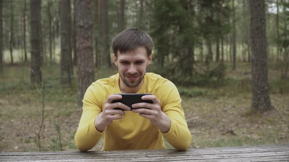 Charming Positive Guy is Satisfied with Process of Mobile Game on Smartphone