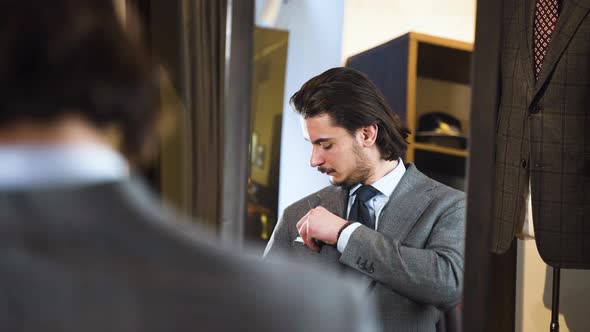 Young bearded man trying on suit in front of fashion boutique mirror.