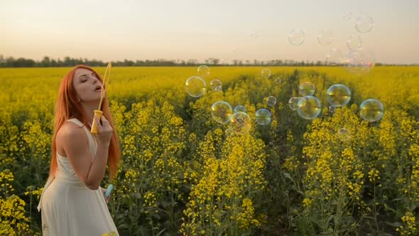 Young Redhair Woman Blowing Bubbles at the Camera Outdoors in Summer Meadow