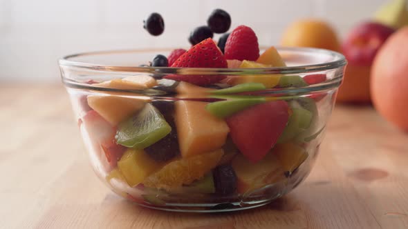 Camera follows putting fresh fruit into fruit salad. Slow Motion.