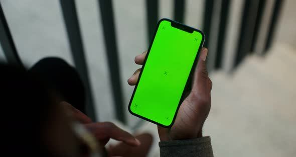 An African American Man Holds a Mobile Phone with a Green Screen in His Hand