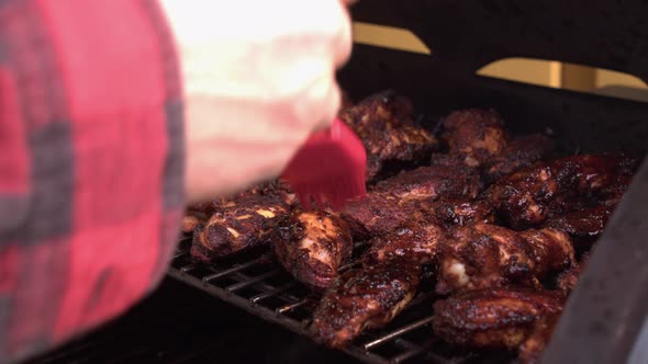 Delicious chicken wings on hot grill are basted with BBQ sauce