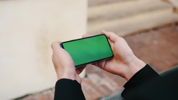 Man Using Smartphone in Horizontal Mode with Green Mock-up Screen Outside Urban City Business Office