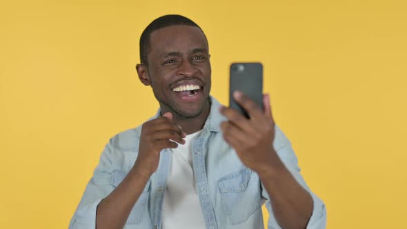 Young African Man Talking for Video Chat Via Smartphone Yellow Background
