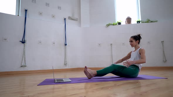 Woman practicing yoga against laptop on mat