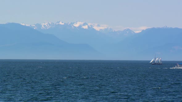 Classic and modern boats crossing in Victoria, BC with Olympic Mountains in the background.