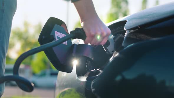 Man plugging in charger into an electric car at charge station. Slow motion