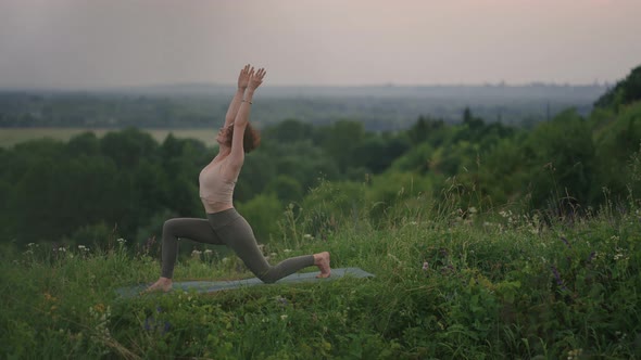 A Young Woman Does Yoga Exercises Standing on the Top of a Forest Mountain Against the Background of