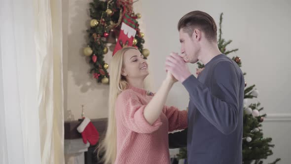 Happy Young Caucasian Couple Dancing in Front of New Year Tree at Home, Smiling Man and Woman in