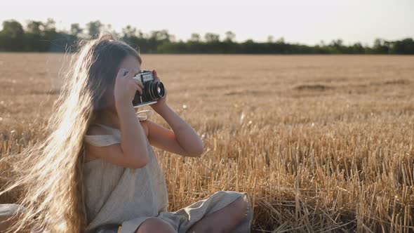 Serious Child Girl with Long Hair Sits on a Mown Wheat Field