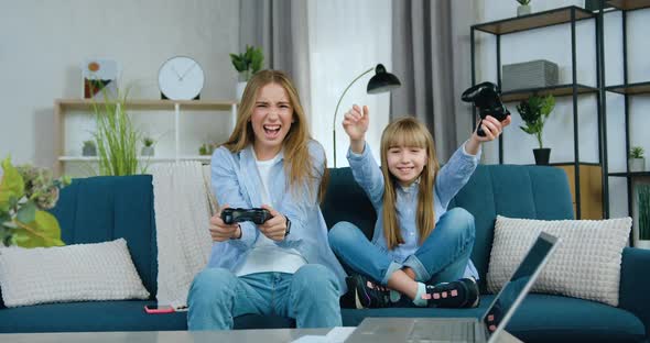 Two Different Ages Girls Playing Video Games Using Joysticks and Celebrating Victory