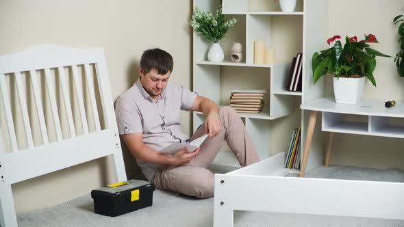 The Man Studies the Instructions for Assembling a Children's Bed