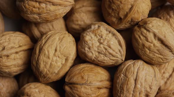 Cinematic, rotating shot of walnuts in their shells on a white surface