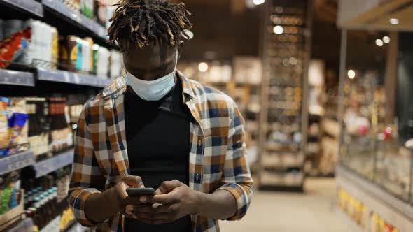 Stylish Man in Mask with Smartphone Walks at the Store Typing on Mobile