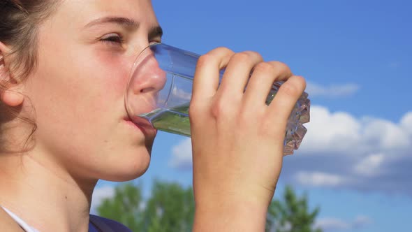 A Teenage Girl Drinking Water Outside on a Sunny Day